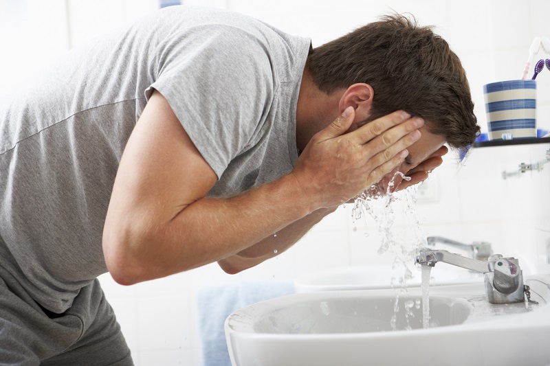Man Washing Face In Bathroom Sink