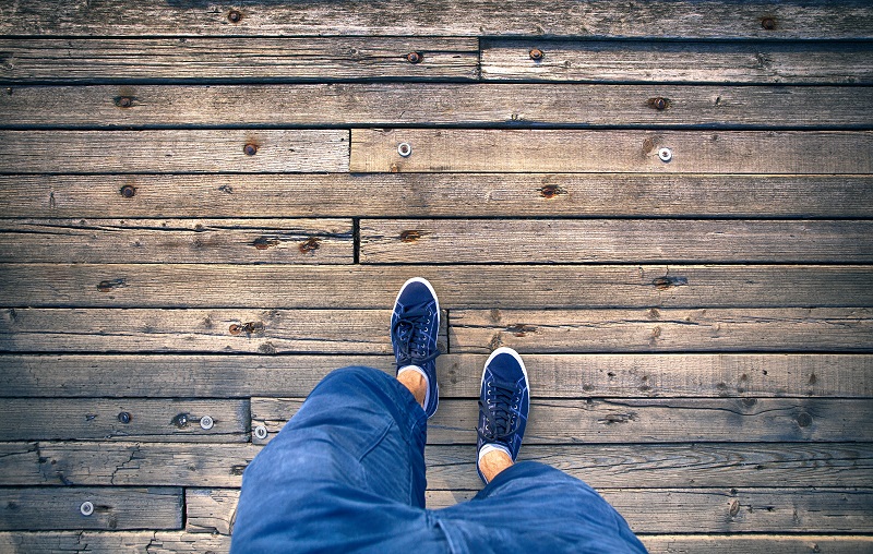 A man walking on aged wooden floor, point of view perspective. A man with blue shoes and shorts jeans walking alone on old wooden bridge. Conceptual photo, point of view perspective used.