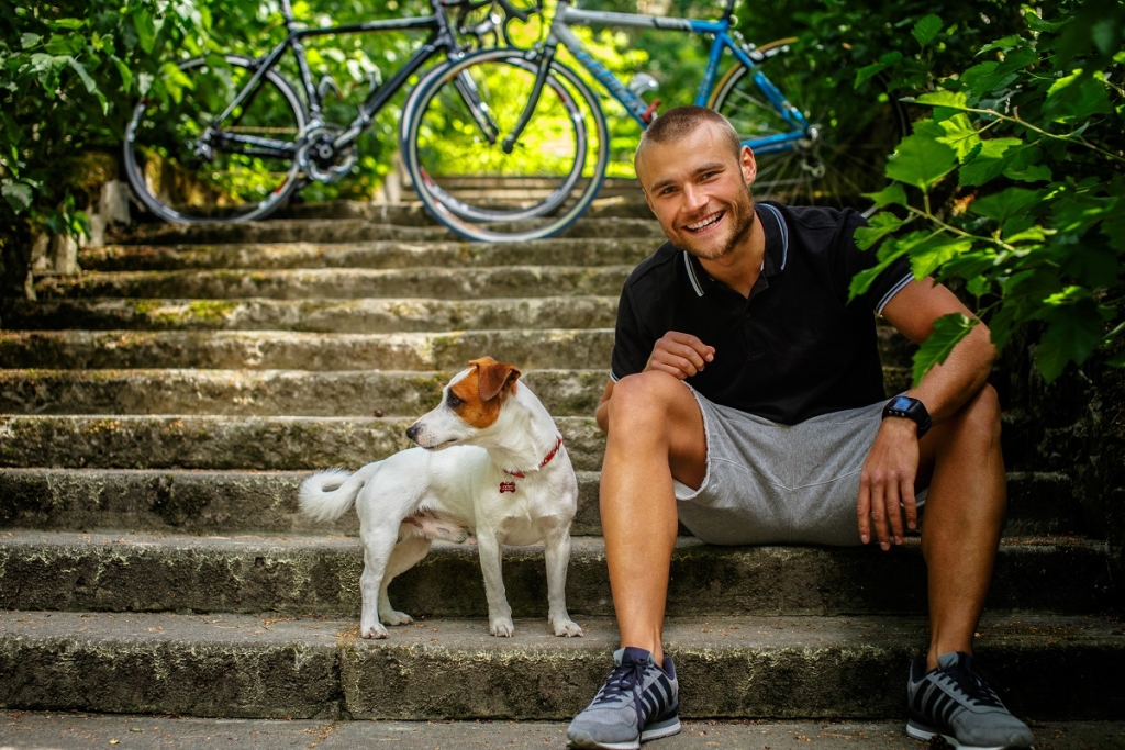 Man with dog sitting on stairs. Bicycles on background.