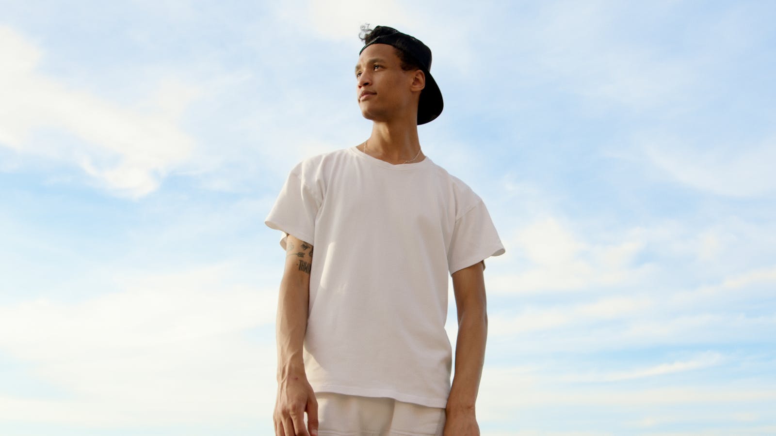 Young Man in Tshirt and Cap against White Clouds