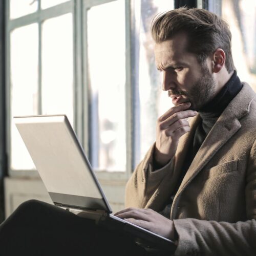 Man Wearing Brown Jacket and Using Grey Laptop