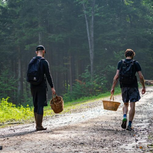 Two men walking down a dirt road with baskets